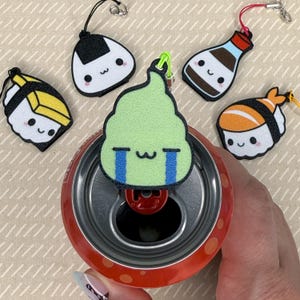 Pu&ograve; includere: Un set di cinque ciondoli portachiavi in feltro colorati a forma di sushi, una bottiglia di salsa di soia e una palla di riso. I ciondoli sono attaccati a una lattina con un anello di apertura rosso.