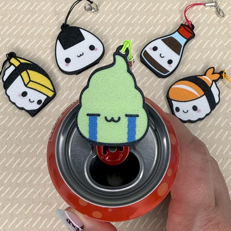 Pu&ograve; includere: Un set di cinque ciondoli portachiavi in feltro colorati a forma di sushi, una bottiglia di salsa di soia e una palla di riso. I ciondoli sono attaccati a una lattina con un anello di apertura rosso.