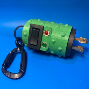 May include: A green electrical outlet with a black switch and red and green indicator lights. The outlet is attached to a black carabiner.