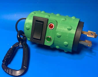 May include: A green, cylindrical, textured electrical plug adapter featuring a black rocker switch, a red indicator light, and a green indicator light. A black metal carabiner is attached to the side of the device via a black ring.