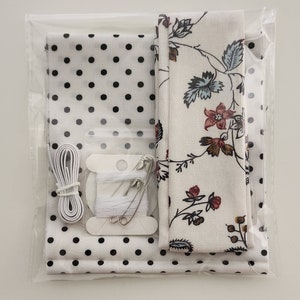 May include: A craft kit containing white fabric with black polka dots, white fabric with a floral pattern, white thread, white elastic and safety pins.