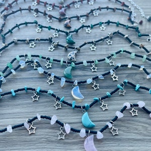 May include: A collection of layered necklaces with black beads, silver star charms, and crescent moon pendants made of various stones, including turquoise, rose quartz, and opal.