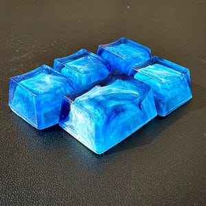 Pu&ograve; includere: Cinque tasti in resina blu con un motivo bianco a spirale. I tasti sono quadrati e hanno una finitura lucida.