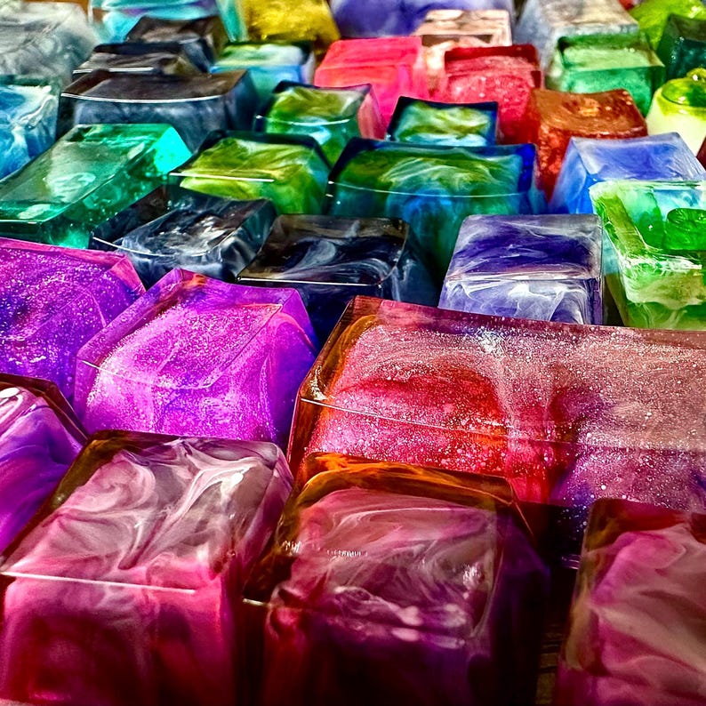 Pu&ograve; includere: Una collezione di tasti per tastiera a forma di cubo, riempiti di resina, con motivi a spirale e glitter. I tasti sono disposti in uno schema casuale, mostrando una variet&agrave; di colori, tra cui viola, rosa, rosso, blu, verde e giallo.