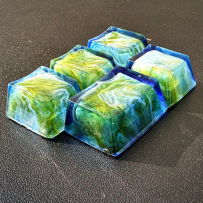 Pu&ograve; includere: Cinque keycap in resina con un designo marmoreo blu, verde e bianco. Le keycap sono di forma quadrata e hanno una finitura lucida.