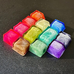 May include: A set of 10 colourful resin keycaps with a swirled pattern. The keycaps are arranged in a triangular shape and are made of a translucent material. The colours include pink, green, blue, purple, brown, yellow, and white.