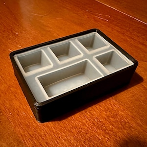 May include: A black plastic storage box with a removable gray silicone insert. The insert has five compartments of different sizes.