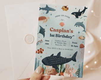 Op de afbeelding: Een blauwe en witte uitnodiging met een aquarel-illustratie van zeedieren. De tekst luidt "Swim on over for Caspian's 1st Birthday". De uitnodiging bevat de datum, tijd en locatie van het feest.