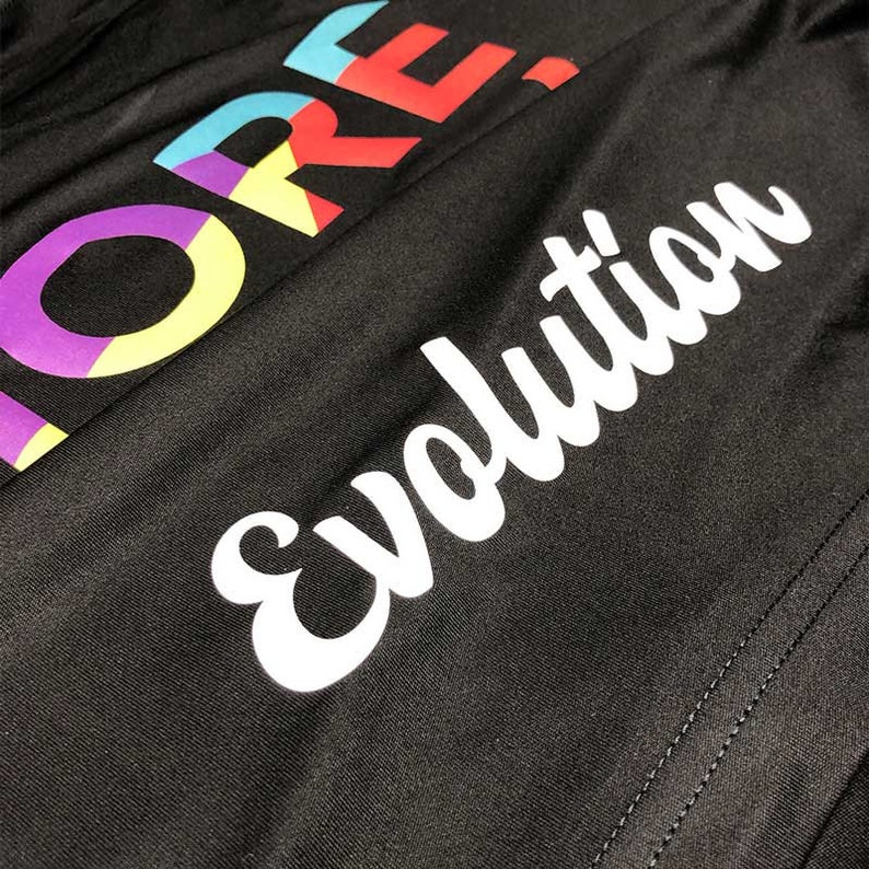 May include: Black fabric with the word "MORE" in colorful block letters and the word "Evolution" in white script. The fabric has a subtle texture and a seam running along the right side.