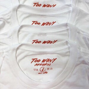 May include: Close-up of several white t-shirts with the text "Too Wavy" printed in red across the upper back. The bottom shirt also displays "Too Wavy Apparel", a size "L" symbol, and "100% cotton".