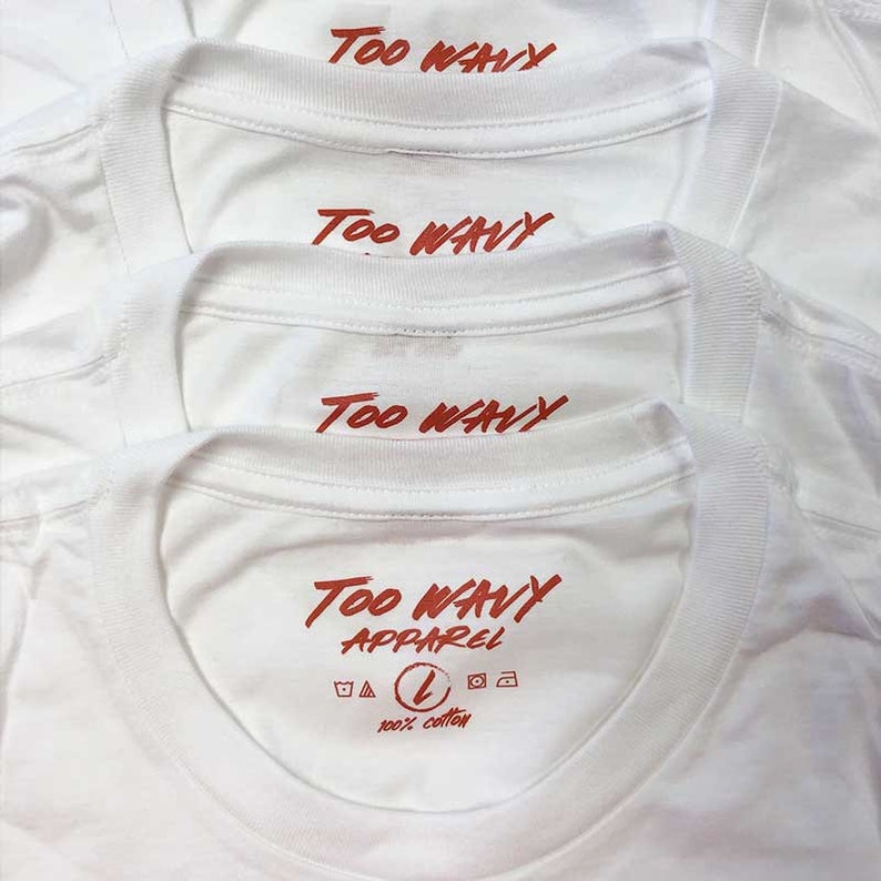 May include: Close-up of several white t-shirts with the text "Too Wavy" printed in red across the upper back. The bottom shirt also displays "Too Wavy Apparel", a size "L" symbol, and "100% cotton".