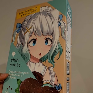 May include: A box of thin mints featuring an anime character with blue eyes and green hair. The box is light blue and yellow with the text "thin mints" and "Crispy chocolate ghosts dipped in mint's ectoplasm" on the front. The box also has a QR code and the text "now Bustin in your mouth!" on the front.