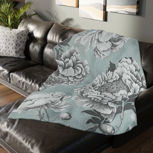 May include: A soft, blue and white throw blanket with a floral pattern. The blanket is made of a soft, plush material and features a large floral design with peonies and leaves.