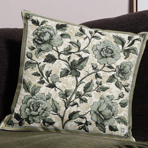 Könnte beinhalten: Ein dekoratives Kissen mit einem floralen Muster mit grünen Blumen und Blättern auf cremefarbenem Hintergrund. Das Kissen hat einen grünen Rand.