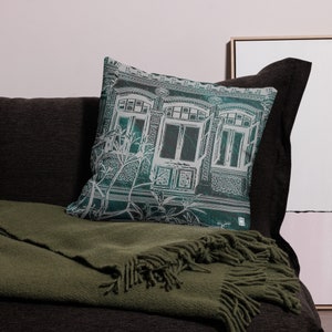 May include: A teal green throw pillow with a white graphic print of a building with windows and ornate details.