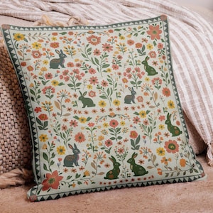 Puede incluir: Una almohada verde y blanca con un patrón floral y conejos. La almohada tiene un borde verde con un patrón geométrico.