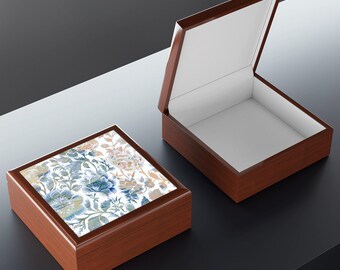 Puede incluir: Una caja de recuerdos cuadrada de madera con acabado marrón oscuro y tapa abatible. La parte superior de la caja cerrada presenta un azulejo decorativo con un patrón floral azul, beige y blanco. Una caja abierta idéntica se sitúa al lado.