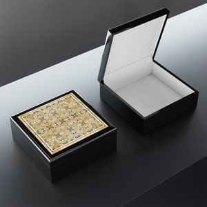 May include: Two black wooden boxes with a decorative pattern on the top of one. The box on the left is closed and the box on the right is open.