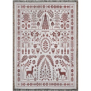 May include: A woven throw blanket featuring a cream-colored base with a dark red folk-art pattern. The design includes symmetrical floral motifs, stylized trees, birds, and two deer facing each other at the bottom, all framed by a decorative border.