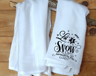 May include: Two white kitchen towels with black text. One towel says "Let it Snow... somewhere else".