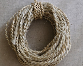 May include: A close-up of a coil of natural fiber rope, likely made of jute or sisal, with a light brown color. The rope is coiled in a circle and has a rough, textured surface.