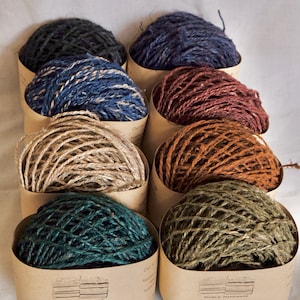 May include: An assortment of colorful twine balls in cardboard containers. The twine is in shades of navy, blue, brown, tan, teal, and olive green. Each container has a label that reads "HUMLA HANDMADE natural fibers made in Nepal."