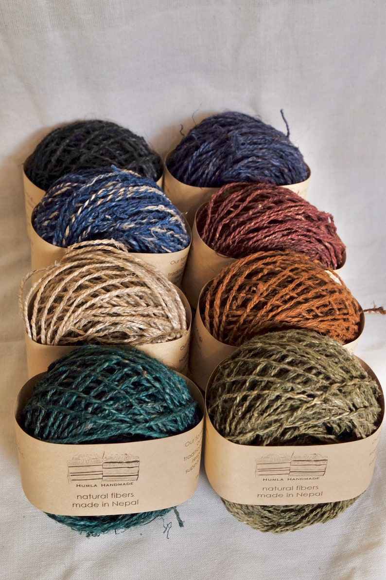 May include: An assortment of colorful twine balls in cardboard containers. The twine is in shades of navy, blue, brown, tan, teal, and olive green. Each container has a label that reads "HUMLA HANDMADE natural fibers made in Nepal."