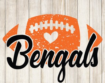 Puede incluir: Diseño gráfico naranja y negro con forma de balón de fútbol, un corazón y la palabra "Bengals" en fuente cursiva. El diseño tiene un aspecto envejecido y vintage, sobre un fondo de vetas de madera clara.