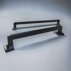 May include: Two dark bronze cabinet pulls with a rectangular base and a straight bar. The pulls are a modern design, suitable for drawers or cabinets. The hardware is made of metal and has a matte finish.
