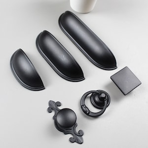 May include: A set of black cabinet hardware, including drawer pulls, knobs, and a ring pull. The hardware has a classic, traditional style.