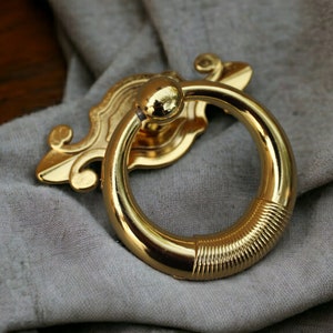 Op de afbeelding: Goudkleurige metalen ringtrekker met een decoratief ontwerp. De ring is glad en heeft een getextureerde rand.