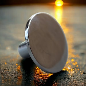 Może przedstawiać: Srebrny, okrągły, płaski pierścień metalowy z gładką powierzchnią. Pierścień leży na teksturowanej powierzchni z rozmytym tłem zachodu słońca.