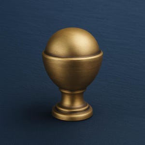 Puede incluir: Un terminal decorativo de color lat&oacute;n, con una parte superior redondeada y una base acampanada. El acabado met&aacute;lico es liso. El terminal est&aacute; dise&ntilde;ado para el montaje en barra. La forma recuerda a un huevo estilizado. Altura aproximada 10 cm.