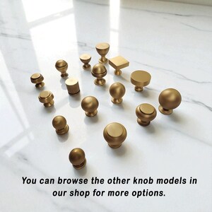 Puede incluir: Una colecci&oacute;n de varios pomos de armario dorados en diferentes formas y tama&ntilde;os. Los pomos incluyen dise&ntilde;os redondos, cil&iacute;ndricos y cuadrados. La imagen incluye el texto: "You can browse the other knob models in our shop for more options."