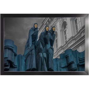 May include: Three statues of women wearing blue robes and gold masks stand on a stone base. The statues are in front of a building with white walls and windows.