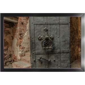 May include: A close-up of a large, dark metal door with a heavy, ornate iron handle. The door is slightly ajar, revealing a brick wall and a set of stairs behind it.