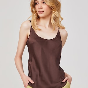 Könnte beinhalten: Ein braunes Camisole-Top mit dünnen Trägern. Das Oberteil hat eine seidige Textur und einen Rundhalsausschnitt. Das Model trägt das Oberteil mit einer gelben Hose. Das Oberteil ist einfarbig und scheint aus leichtem Material zu sein.