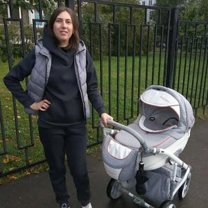 May include: A grey and white baby stroller featuring a protective canopy with the text 'AVENIR' in orange, a matching storage bag attached to the handle, and a white frame with four wheels, designed for transporting an infant in a seated position.