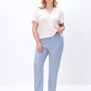Puede incluir: Una blusa de color crema con cuello en V y mangas cortas combinada con pantalones azul claro. La blusa presenta un corte relajado con mangas cortas, mientras que los pantalones son de corte recto con una apariencia limpia y sencilla.