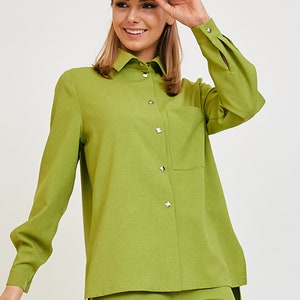 May include: A lime green long-sleeve button-down shirt featuring a pointed collar, a single chest pocket, and silver-toned pyramid-shaped studs on the front placket and cuffs. The shirt is paired with matching lime green trousers and a white baseball cap.