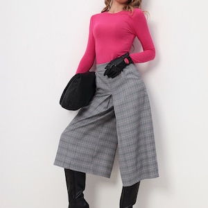 May include: A woman in a fuchsia long-sleeved top, grey plaid culottes, black gloves, and knee-high black boots. She wears black sunglasses and carries a black bag. The outfit is set against a white background.