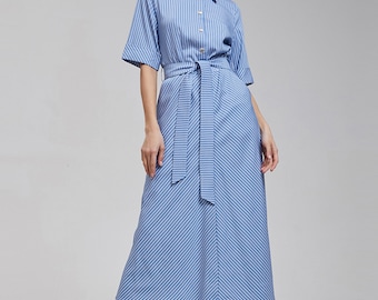 Puede incluir: Un vestido camisero de largo midi con rayas verticales en azul claro y blanco. El vestido presenta un cuello clásico, cierre frontal de botones, mangas a la altura del codo con puños doblados y un cinturón de tela a juego en la cintura.