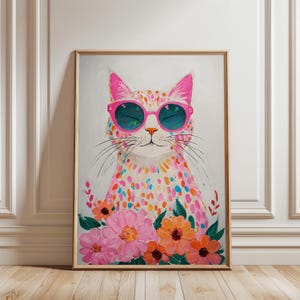 May include: A framed art print featuring a colorful cat wearing pink sunglasses. The cat is covered in a pattern of colorful dots and is surrounded by pink and orange flowers. The artwork is displayed on a white wall and wooden floor.