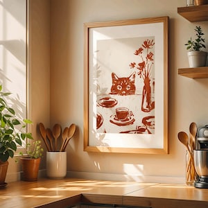 May include: A framed print featuring a cat peering over a table set with a coffee cup, plates, and a vase of flowers. The artwork is in shades of brown and cream, with a wooden frame. The scene evokes a cozy, vintage aesthetic.