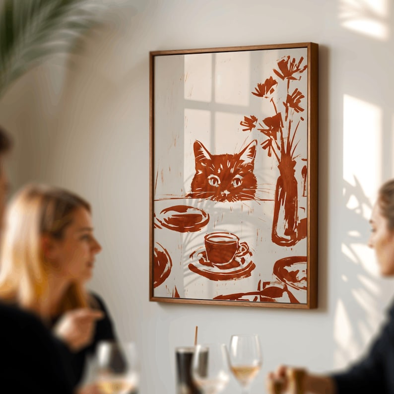 May include: A framed wall art print featuring a cat peering over a table set with a cup and saucer, plates, and a vase of flowers. The artwork is in shades of brown and white, with a wooden frame.