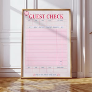 May include: A framed pink guest check with a gold frame. The text "GUEST CHECK" is at the top, with fields for date, table, guests, server, and check number. Below are sections for appetizers, soup, entree, vegetables, dessert, and beverages. The bottom reads "THANK YOU. PLEASE COME AGAIN."