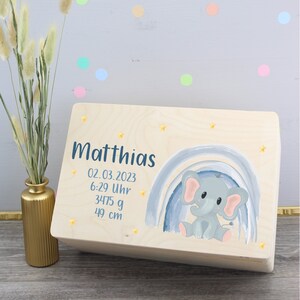 Könnte beinhalten: Eine Holz-Erinnerungskiste mit einem hellblauen und grauen Aquarell-Regenbogen und einem grauen Elefanten. Die Kiste ist personalisiert mit dem Namen "Matthias", dem Datum "02.03.2023", der Uhrzeit "6:29 Uhr", dem Gewicht "3475 g" und der Länge "49 cm".