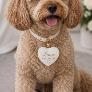 May include: A light brown dog wearing a white leather collar with a heart-shaped tag. The tag reads "Luna RING BEARER" in gold lettering. The dog is sitting and has its tongue out. The words "Ready for the Aisle" are at the bottom.