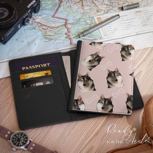 May include: A black passport holder with a pink passport cover featuring a repeating pattern of a dog's face and white bone. The passport cover has the text "Ready for the Aisle" in white.