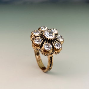 May include: A gold ring with a flower-shaped design featuring clear rhinestones.